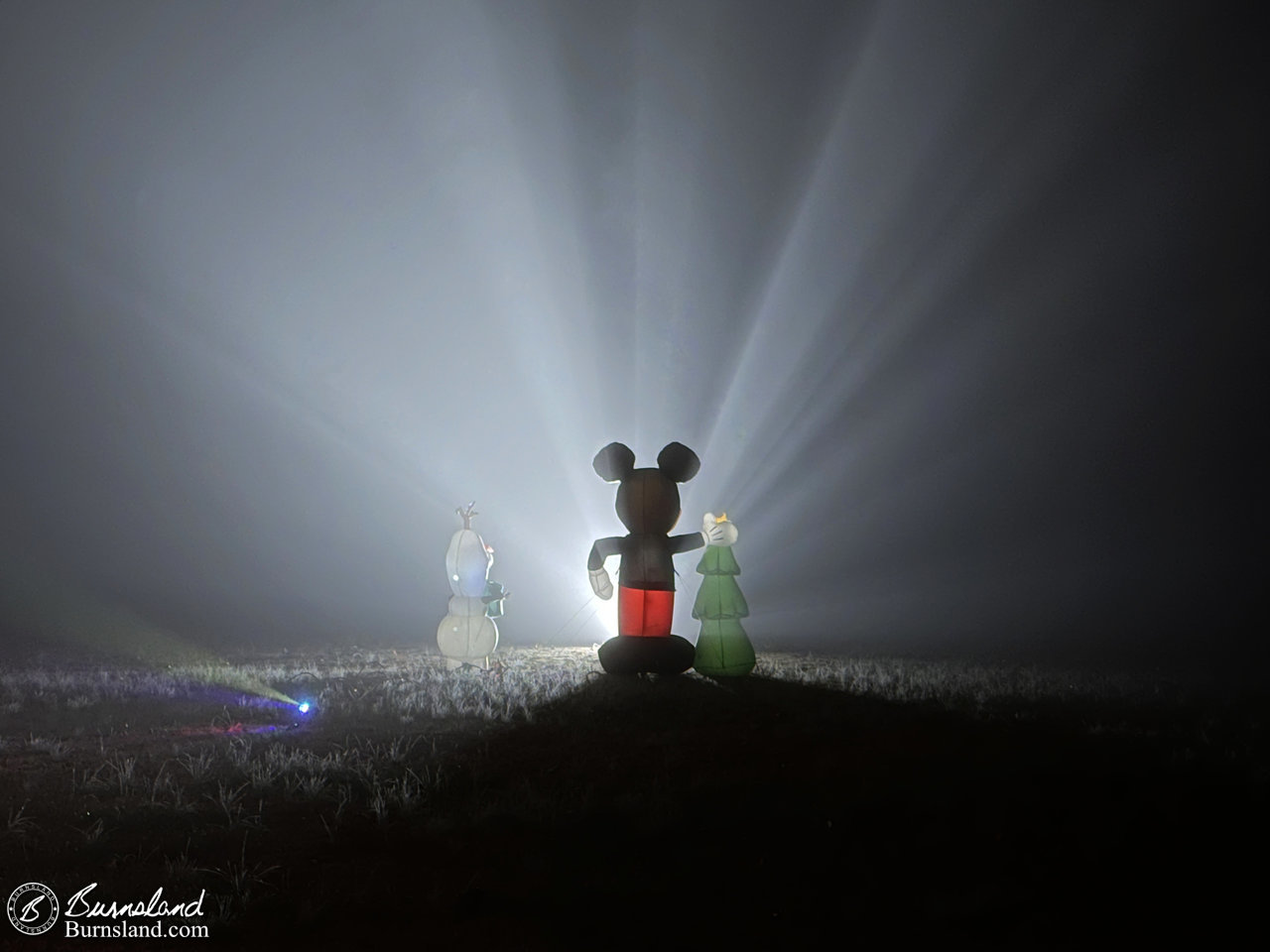 Christmas inflatables of Mickey Mouse and Olaf from Frozen are highlighted by a spotlight on a foggy evening in our front yard.